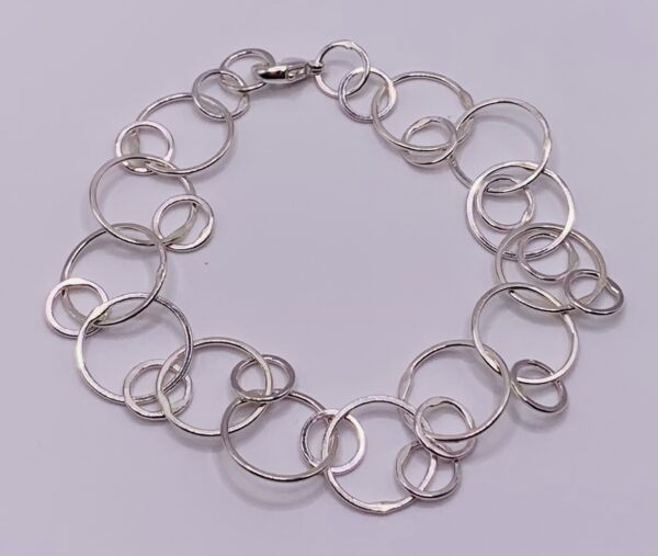 Handmade sterling silver bracelet with small link charms photographed against a lilac background