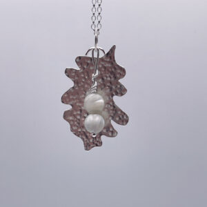 Unique handmade textured leaf pendant with two white mother of pearl beads hanging down in front of the leaf. The pendant hangs on a silver trace chain. On a white background.