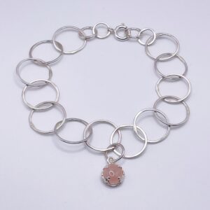 Delicate handmade bracelet made from hammered recycled sterling silver circular links. Fastened with a silver bolt ring. Am 8mm rose quartz cabochon is encased in a filigree bezel setting and attached to the middle link of the bracelet to add a touch of colour. On a white background.